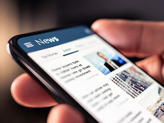 person's hand holding smartphone showing news page